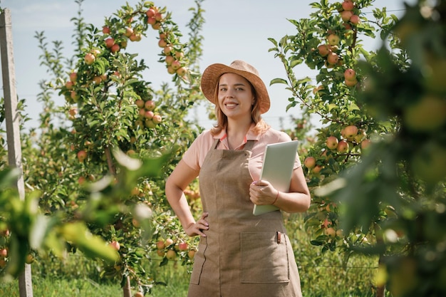 Attraktive Agronomin oder Landwirtin mit Laptop, die im Apfelgarten steht und Obst überprüft, macht sich Notizen Landwirtschafts- und Gartenkonzept Gesunde Ernährung