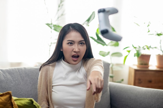 Attraktive Asiatin wirft einen Videospiel-Joystick, weil sie im Wohnzimmer ein Streichholz verliert und wütend ist