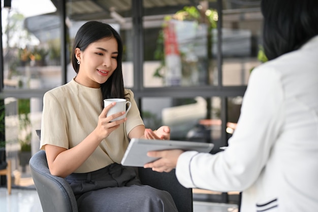 Attraktive asiatische CEO bei einem informellen Treffen mit ihrer Sekretärin im Büro