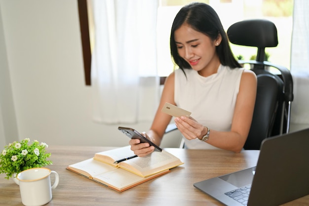 Attraktive asiatische Frau, die eine Kreditkarte und ein Smartphone mit einer mobilen Banking-App hält