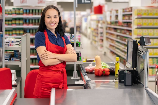 Attraktive asiatische Frau, die im Supermarkt an der Kasse mit verschränkten Armen steht