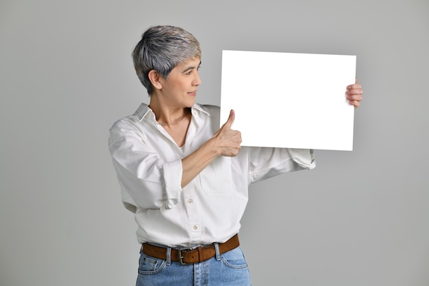 Attraktive asiatische Frau mittleren Alters, die leeres Schild isoliert auf weißem Hintergrund zeigt