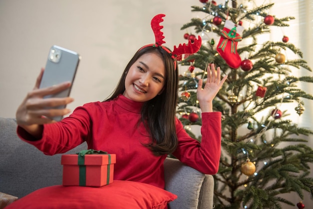 Attraktive asiatische Frau Videoanruf Gespräch über Smartphone Gruß Weihnachten Neujahr Weihnachtsbaum Hintergrund