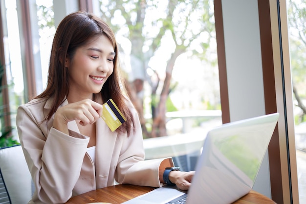 Attraktive asiatische Geschäftsfrau, die Kreditkarte für Warenzahlungen verwendet, die online per Laptop im Café einkaufen Selbstbewusste und intelligente Frau und Geschäftskonzept