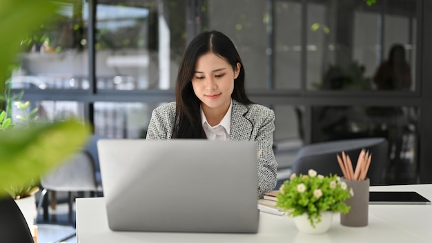 Attraktive asiatische Geschäftsfrau, die sich auf ihr Projekt konzentriert und an ihrem Schreibtisch im Büro arbeitet