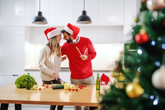 Attraktive blonde Frau, die Gurke schneidet, während ihr Freund sie umarmt