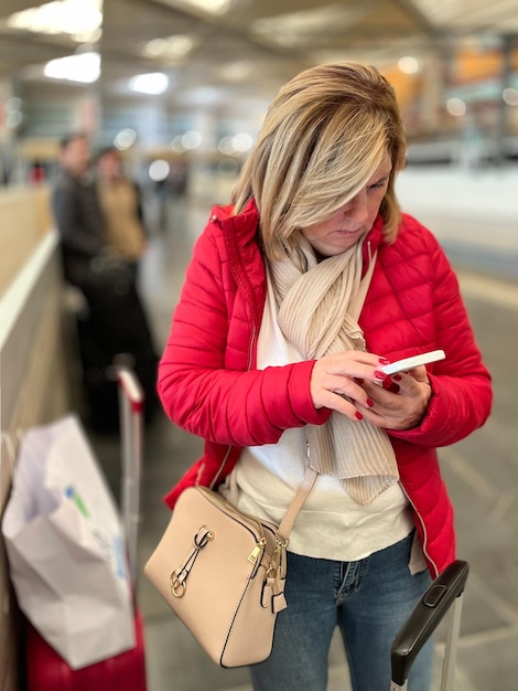 Attraktive blonde Frau, die mit dem Handy am Bahnhof wartet