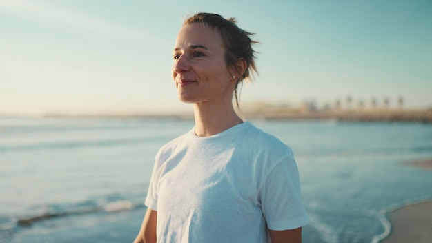 Attraktive, blonde Frau, die nach der Yoga-Praxis glücklich zu Fuß am Meer entlang schaut Hübsches Mädchen, das einen guten Start in den Tag am Strand genießt