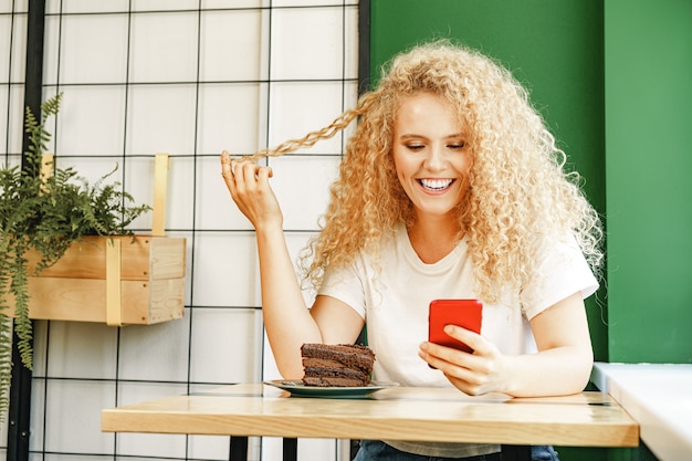 Attraktive blonde Frau, die nahe Fenster im Café sitzt und ihr Handy benutzt