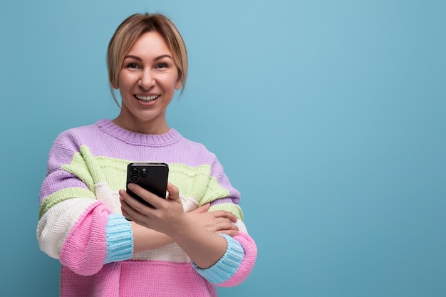 Attraktive blonde Frau im lässigen Look demonstriert das Chatten in einem Smartphone auf blauem Hintergrund