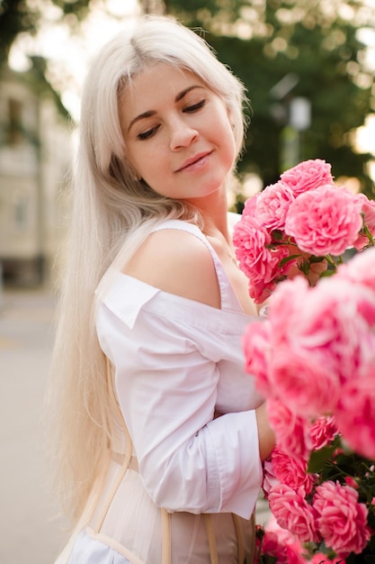 Attraktive blonde Frau mit rosa Rosenblüten im Park im Freien