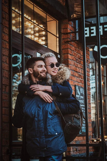 Attraktive blonde Frau mit Sonnenbrille umarmt ihren gutaussehenden Mann auf der Straße.