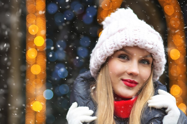 Attraktive blonde Frau trägt Strickmütze zu Fuß auf der Wintermesse bei Schneefall. Leerer Platz für Text