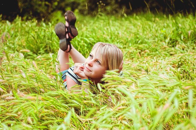 Attraktive blonde junge Frau, die sich entspannt, im Feld sitzt, Park mit grünem Gras im Sommer