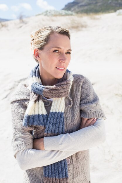 Attraktive blonde Stellung auf dem Strand im woolen Schal