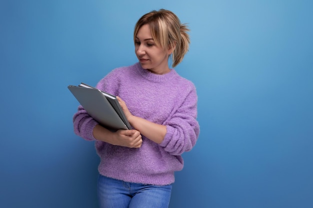 Attraktive blonde tausendjährige Frau mit Laptop für die Arbeit auf blauem Hintergrund