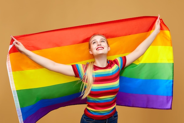 Attraktive Blondine posierte mit einer Regenbogen-LGBT-Flagge. Fotoshooting im Studio auf gelbem Hintergrund.