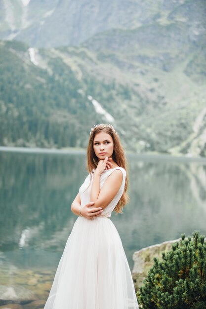 Attraktive brünette Braut in einem wunderschönen weißen Hochzeitskleid, das in der Nähe des Sees Morskie Oko steht