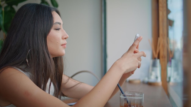 Attraktive Brünette, die eine Handy-App in einer Cafeteria aus der Nähe surft