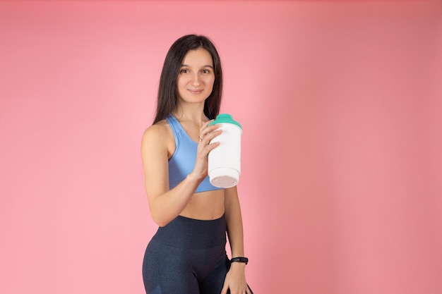 Attraktive Brünette Frau in modischer Sportbekleidung auf rosa Hintergrund Sport Girl Trinkwasser nach Kaugummi Gesunder Lebensstil-Konzept