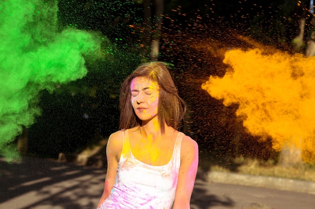 Attraktive brünette Frau mit kurzen Haaren posiert mit explodierender grüner und orangefarbener Holi-Farbe