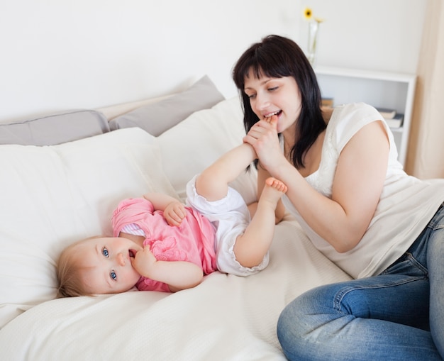 Attraktive Brunettefrau, die mit ihrem Baby beim Lügen auf einem Bett spielt