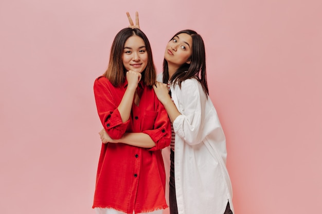 Attraktive charmante asiatische Mädchen haben Spaß und machen lustige Gesichter auf rosa Wand