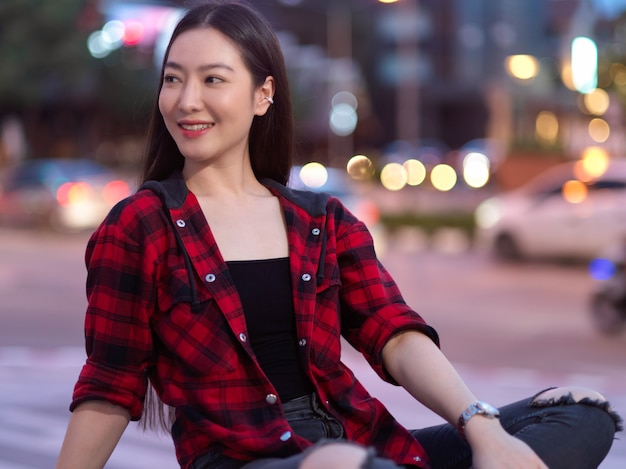 Attraktive elegante junge Frau, die lächelt und von der Kamera wegschaut, die auf der Stadtstraße sitzt