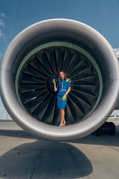 attraktive elegante weibliche Angestellte der Fluggesellschaft, die sich an den Turbofan-Triebwerksspinner lehnt