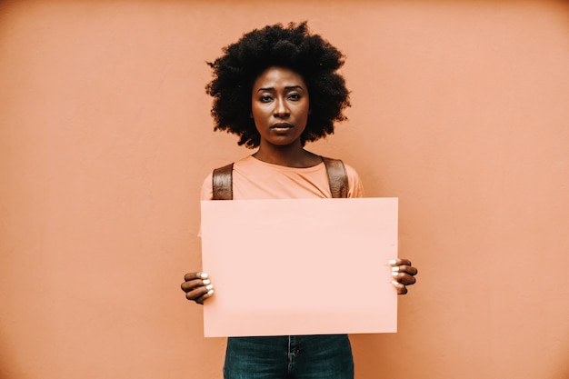 Attraktive ernsthafte afrikanische Frau, die leeres Papier steht und hält.