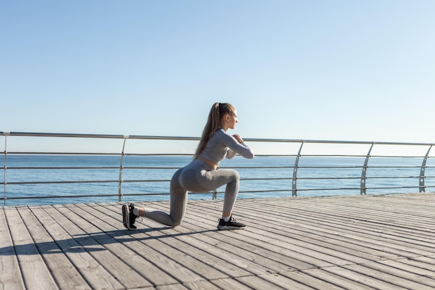 Attraktive, fitte Frau, die an einem hellen, sonnigen Tag Ausfallschritte am Strand praktiziert Gesundes Lebensstil-Training im Freien