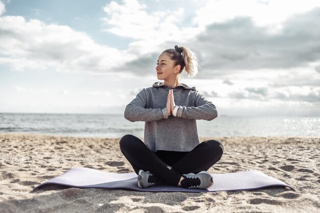 Attraktive, fitte Frau in Sportbekleidung meditiert an einem sonnigen Tag am Strand