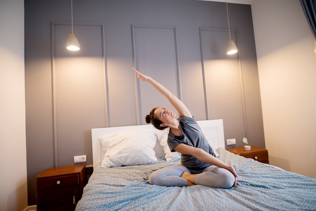 Attraktive form sportliche frau mittleren alters, die sitzende yoga-posen auf dem bett vor dem schlafengehen tut.