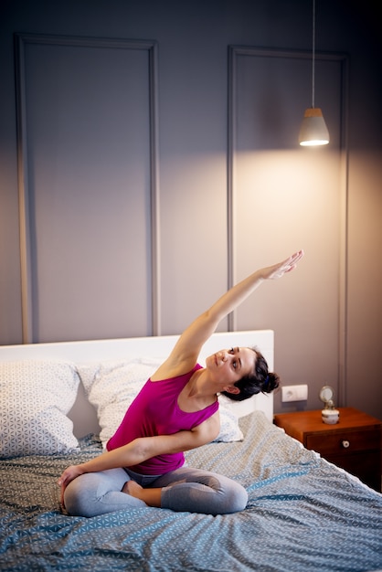 Attraktive Form sportliche Frau mittleren Alters, die sitzende Yoga-Posen auf dem Bett vor dem Schlafengehen tut.