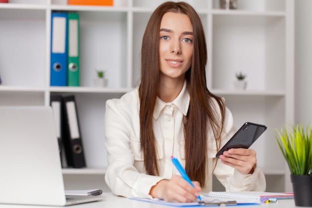 Attraktive Frau, die am Smartphone in ihrer Arbeitsstation arbeitet.