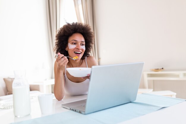 Attraktive Frau, die ihren Laptop beim Frühstück und beim Lernen im Haus drinnen benutzt.