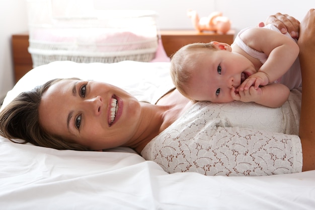 Attraktive Frau, die im Bett mit nettem Baby lächelt