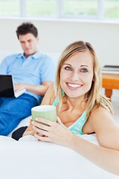 Attraktive Frau, die mit einem Tasse Kaffee hat ihren Freund verwendet einen Laptop im Hintergrund sich entspannt