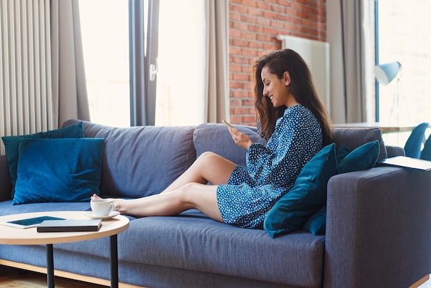 Attraktive Frau, die Tablet im modernen Wohnzimmer zu Hause verwendet und Freizeit im sozialen Chat verbringt