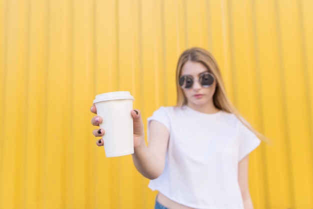 Attraktive Frau hält eine weiße Tasse Kaffee in ihren Händen auf einem gelben