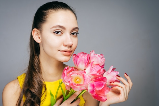 Attraktive Frau im gelben Kleid hält einen Strauß duftender rosa Blumen und lächelt