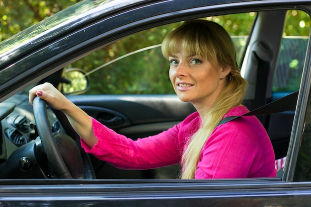 Attraktive Frau im Rosa die Fahrt in ihrem Auto genießend