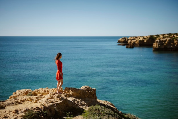 Attraktive Frau im roten Kleid auf Klippen am Sao Rafael Beach Algarve Südportugal