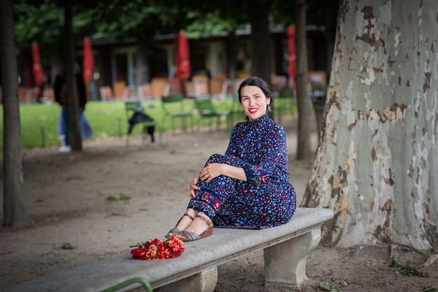 Attraktive Frau in einem blauen Kleid, die im Park sitzt