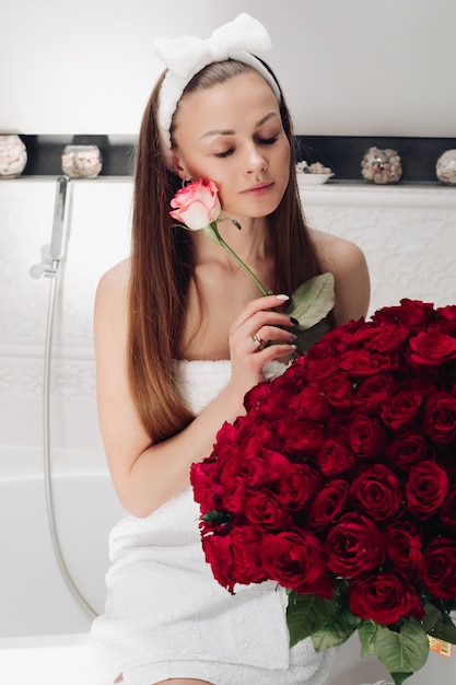 Attraktive Frau in Handtuch und Stirnband mit Strauß roter Rosen