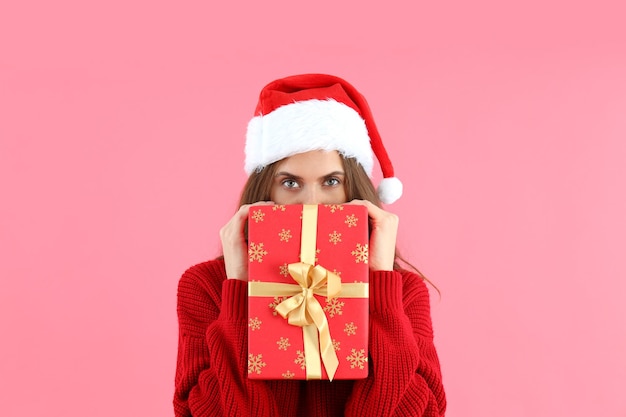 Attraktive Frau in Weihnachtsmütze hält Geschenkbox auf rosa Hintergrund