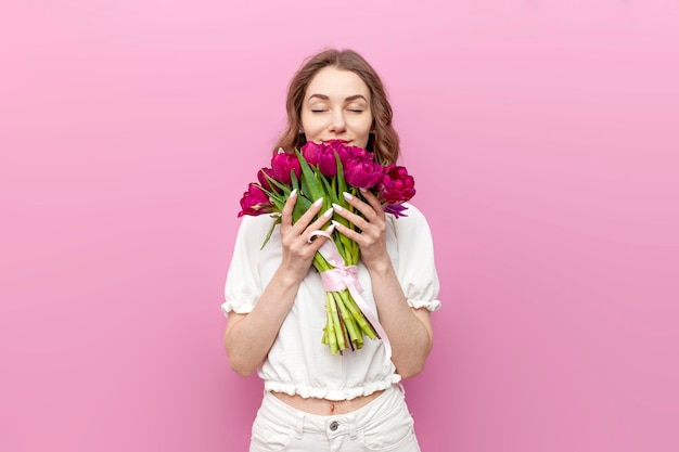 Attraktive Frau in weißer festlicher Kleidung hält einen Strauß rosa Tulpen in der Hand und riecht den Duft