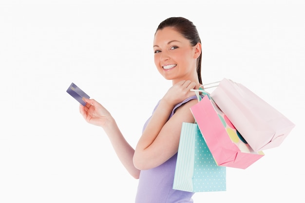 Attraktive Frau mit einer Kreditkarte, die Einkaufstaschen bei der Stellung hält