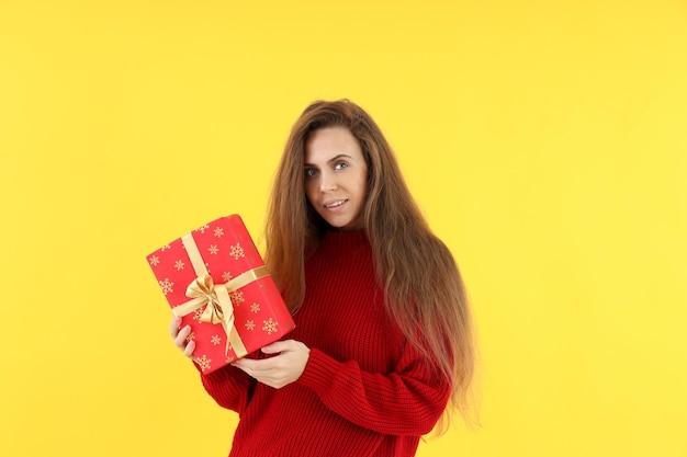 Attraktive Frau mit Weihnachtsgeschenkbox auf gelbem Hintergrund