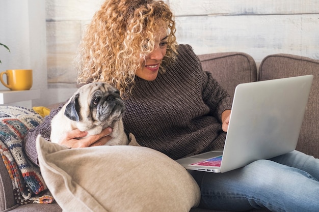 Attraktive Frau mittleren Alters mit ihrem besten Freund alten Hundemops, der zu Hause an einem Laptop arbeitet
